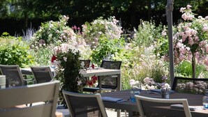 An outdoor dining area with tables and chairs, surrounded by lush greenery and flowering plants. - The Jangle Hotel - Paris - Charles de Gaulle - Airport (Le Mesnil-Amelot)