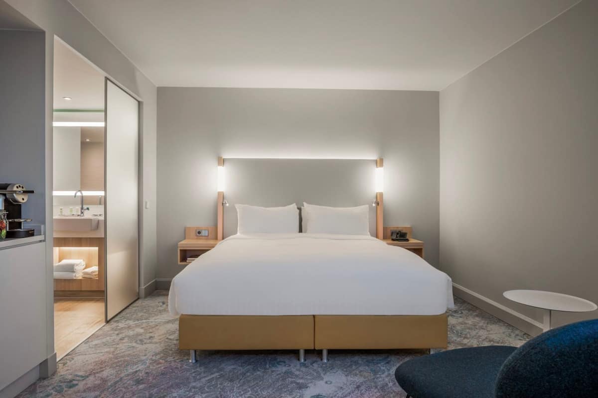 A modern hotel room with a large bed, bedside tables, a small round table, and a walk-in closet.