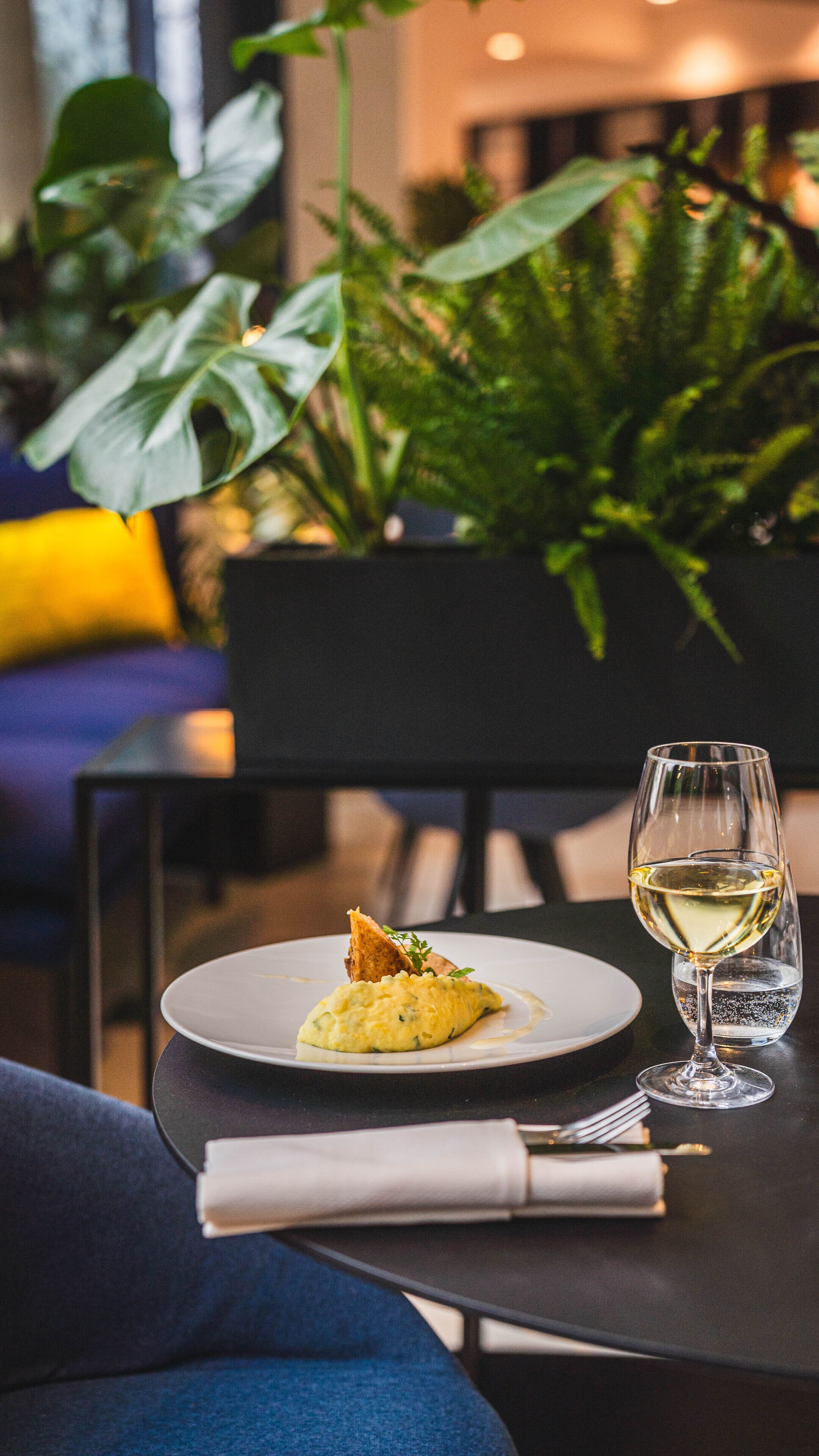 A dining table with a plate of food, a glass of white wine, and a napkin.