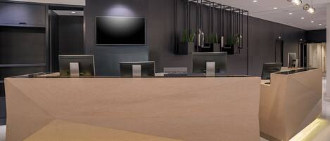 A modern reception desk with a flat-screen TV, multiple computer monitors, and a reception area.