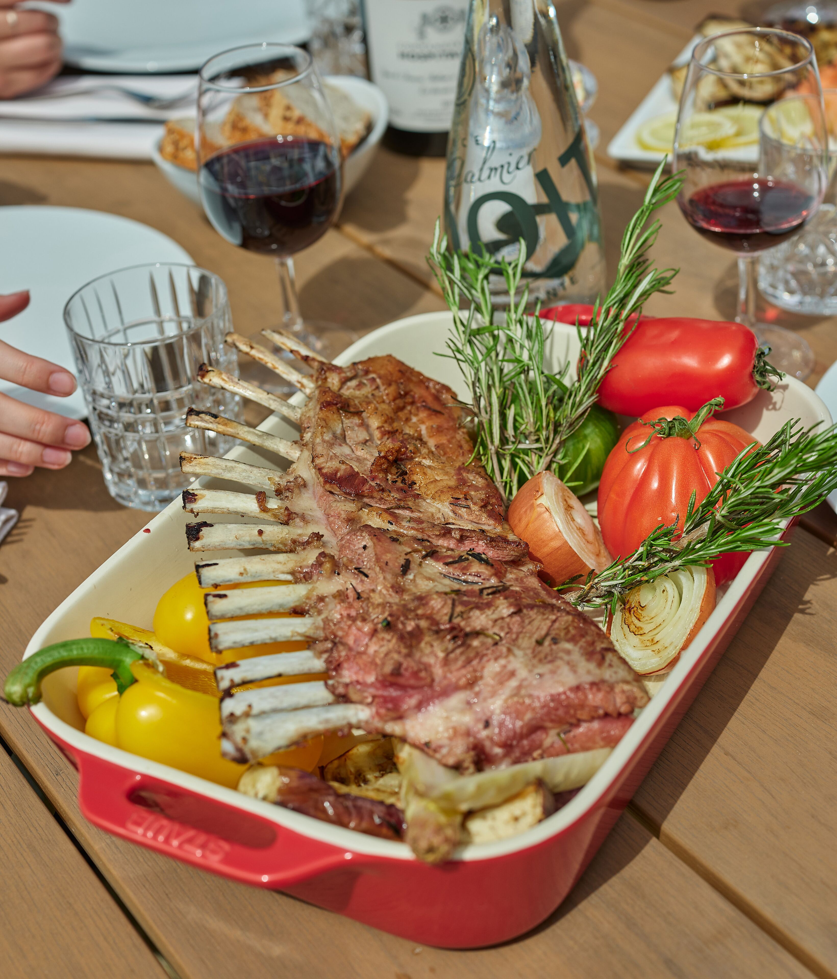 A roasted lamb rack with vegetables and rosemary on a table.