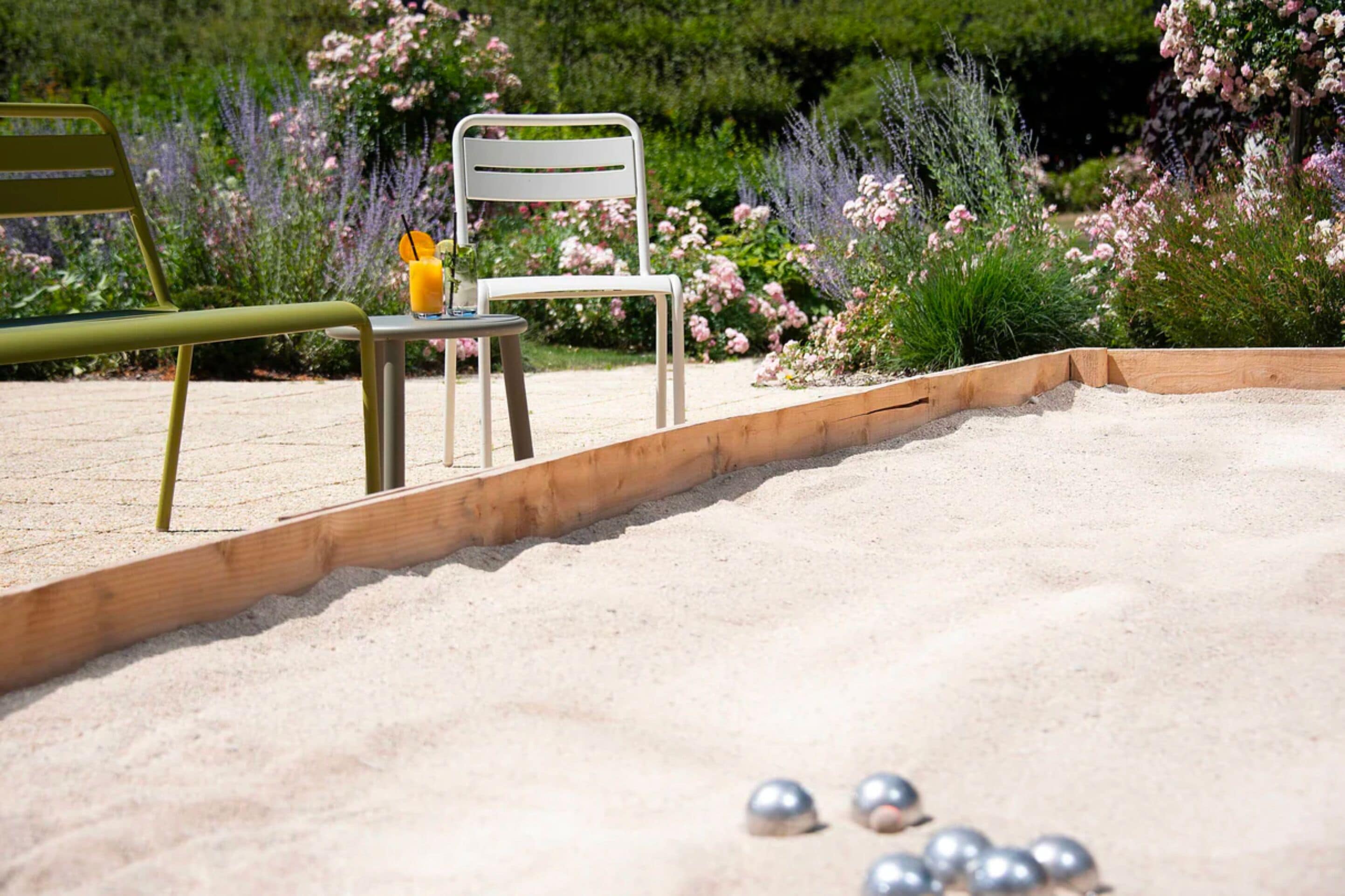 Een tuin met een houten bankje, een stoel en een tafel met drankjes.