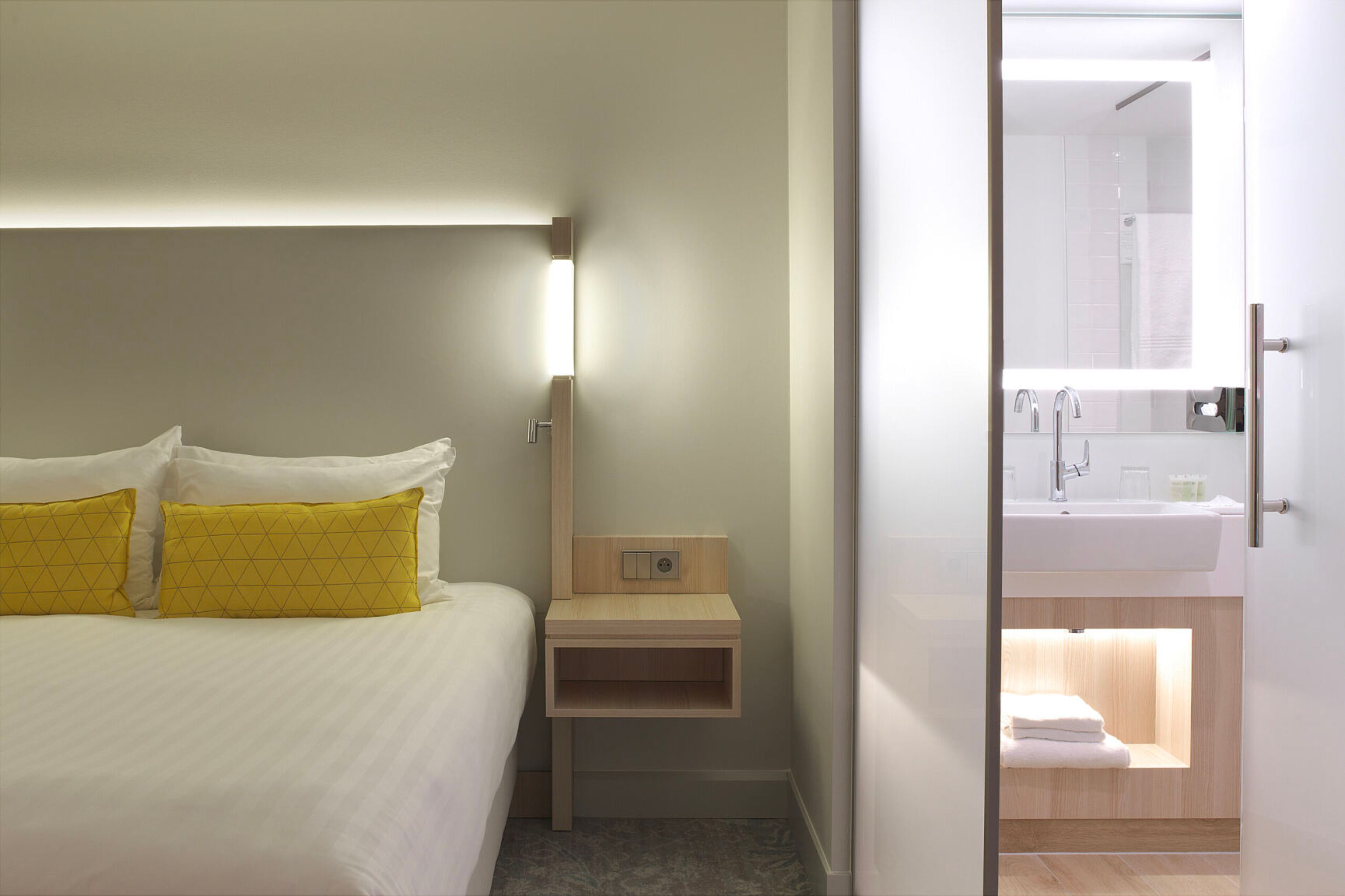 Habitación de hotel con cama, mesita de noche y baño visible a través de una puerta abierta.