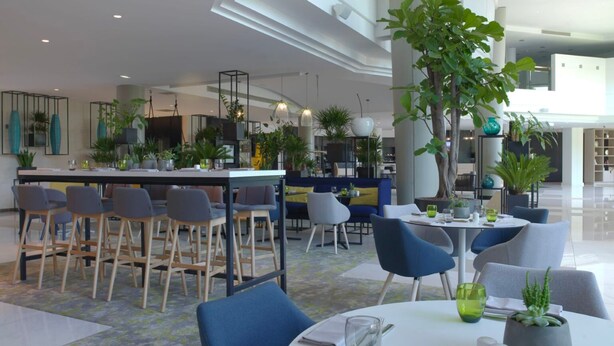 A modern hotel lobby with a bar area, seating arrangements, and indoor plants. - The Jangle Hotel - Paris - Charles de Gaulle - Airport (Le Mesnil-Amelot)