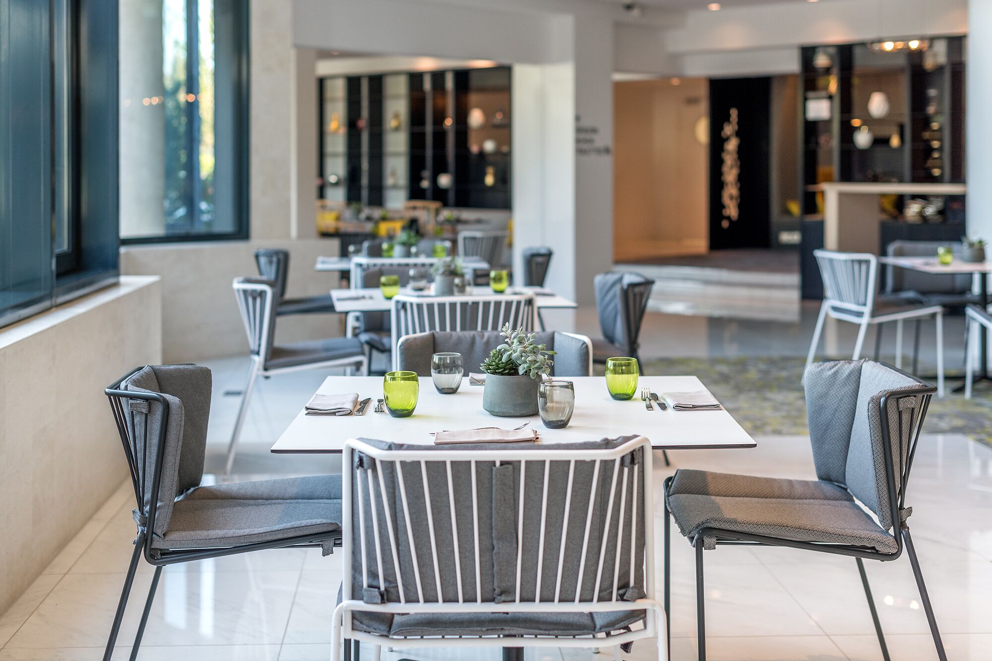 Interior modern d'un restaurant amb taules preparades per dinar, cadires i una planta en test amb posar a la taula.