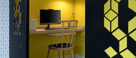 Un espace de travail comprenant un ordinateur, un bureau, une chaise et une lampe, le tout placé devant un mur jaune.