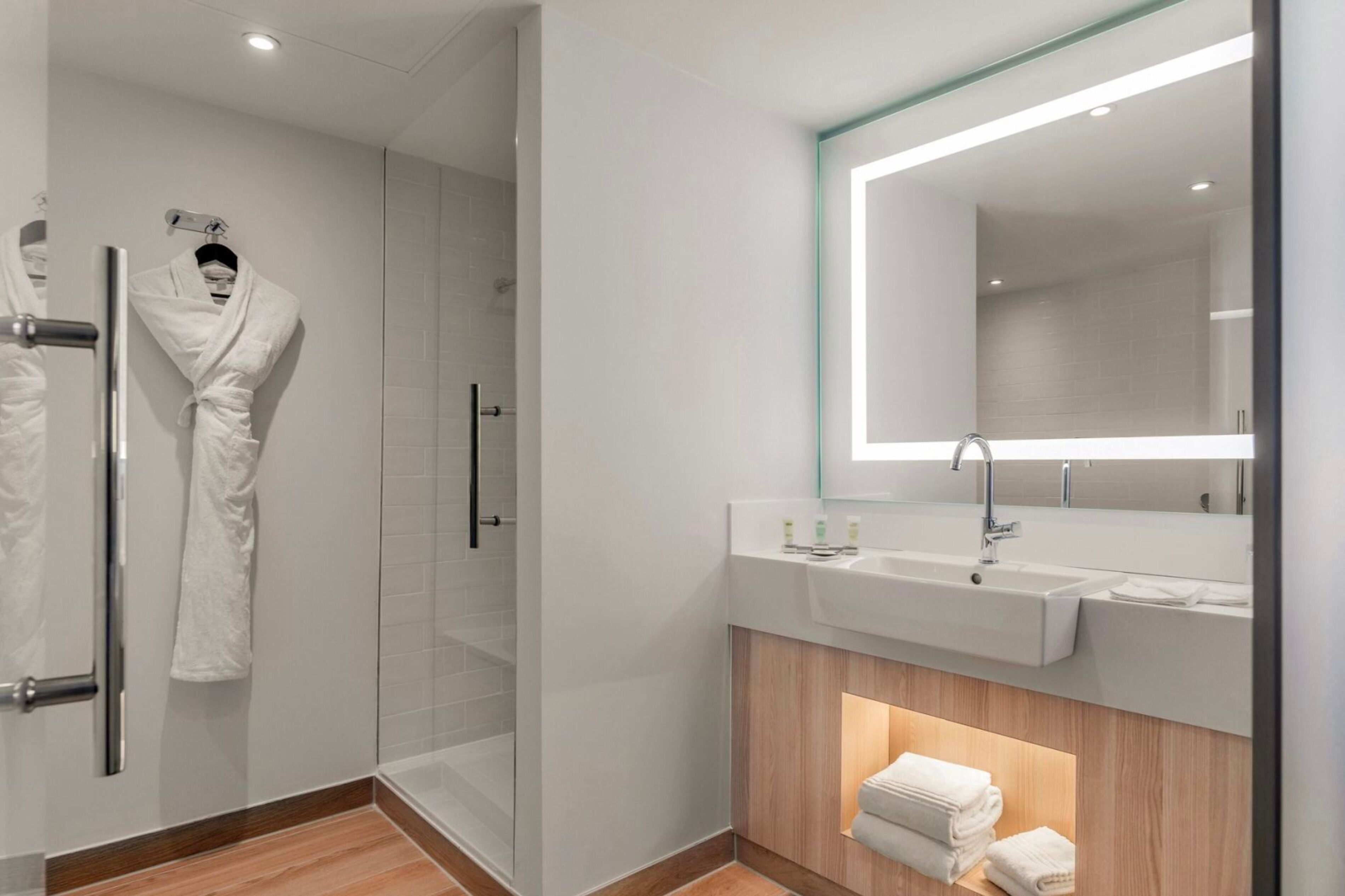 A modern bathroom with a glass shower enclosure, a vanity with a large mirror, and neatly folded towels on the floor.