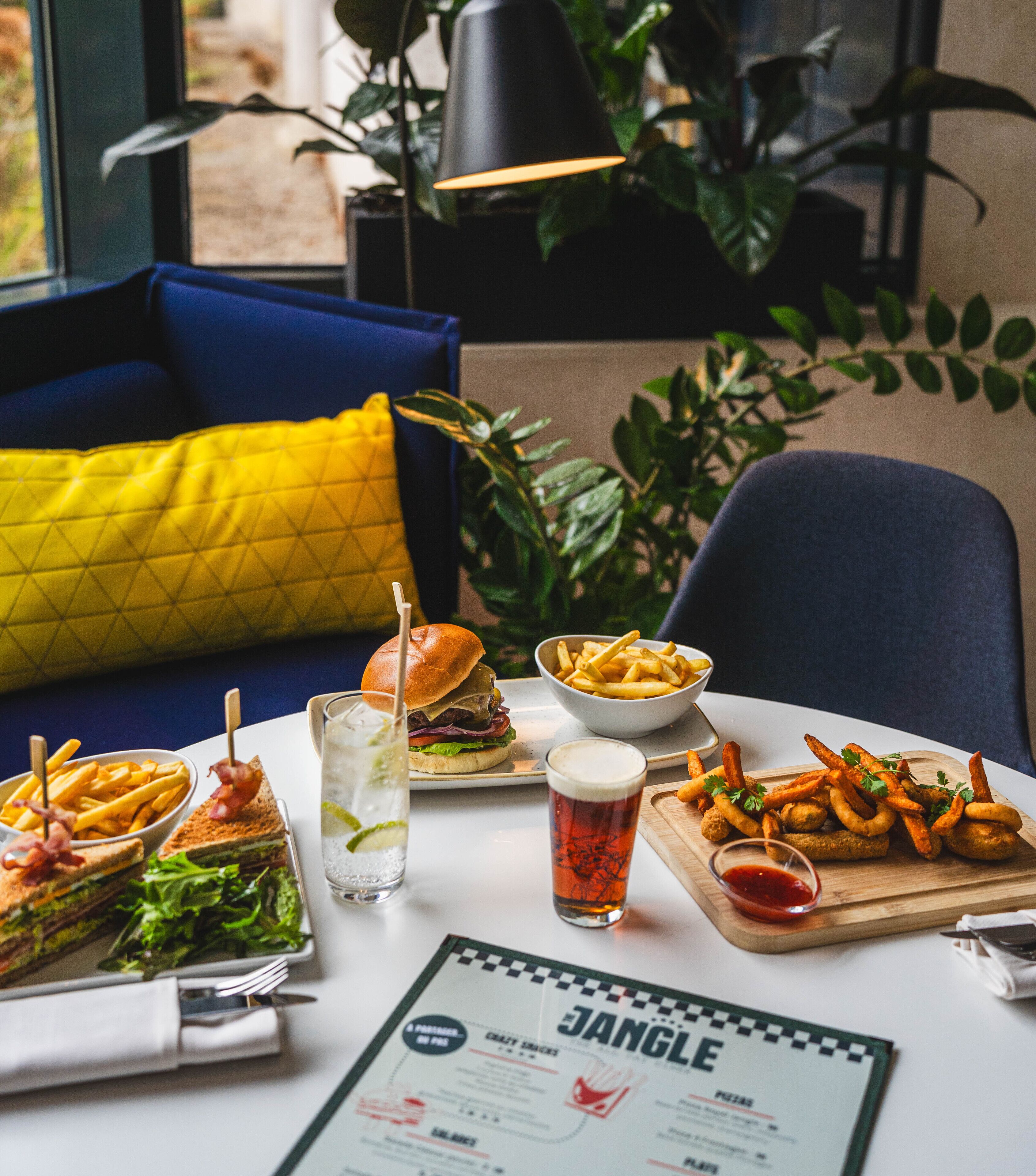 A dining table with a menu, various dishes including a burger, fries, and a salad, and a drink.