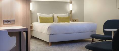 A hotel room with a bed, bedside table, chair, and a desk.