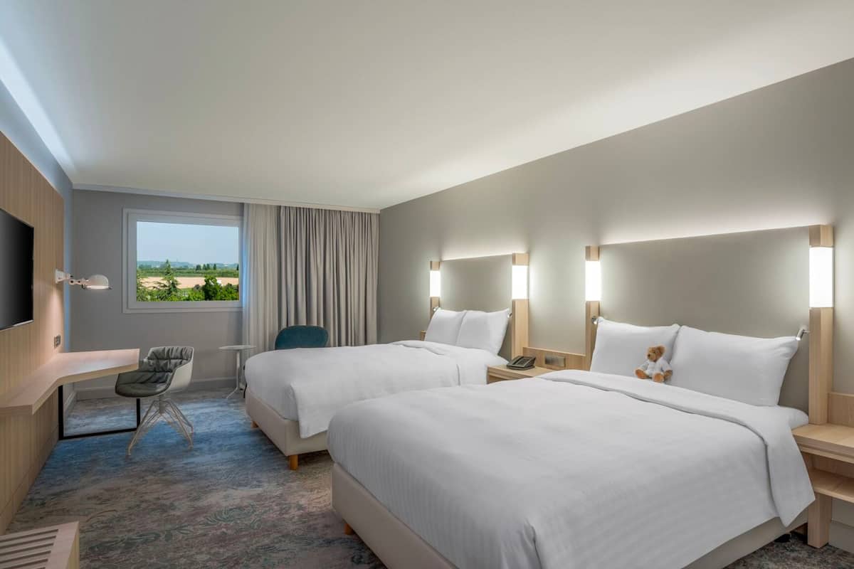 A hotel room with two beds, a desk, a chair, and a TV.