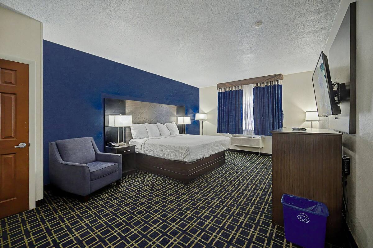 Une chambre d’hôtel avec un lit, une chaise, un bureau, une télévision et une poubelle.