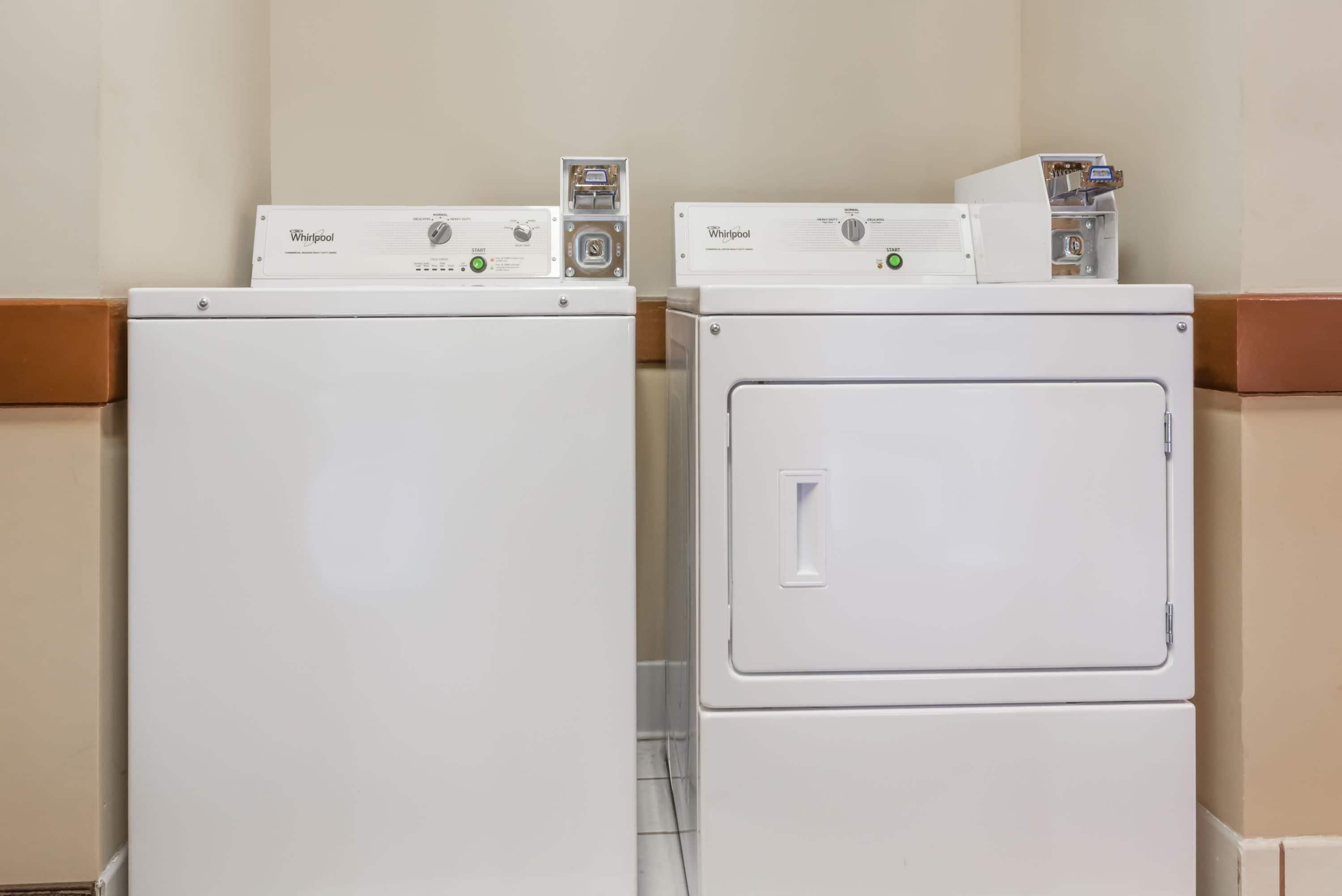 Två tvättmaskiner från Whirlpool, placerade ovanpå varandra, i ett tvättrum med en enkel vägg och en brun sockellist.
