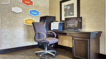 A hotel room with a desk, chair, printer, and a wall with hexagonal signs labeled "enter," "happy," and "zone."