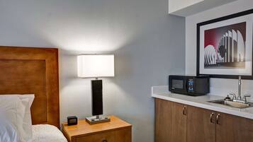 Une chambre d’hôtel équipée d’un lit, d’une lampe de chevet, d’une table de chevet, d’un four à micro-ondes et d’un lavabo.