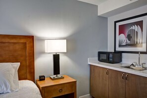 A hotel room with a bed, a bedside lamp, a nightstand, a microwave, and a sink.