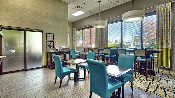 A hotel dining area with tables and chairs, large windows with blinds, and a patterned carpet. - Hampton Inn Norfolk-Naval Base (Norfolk)