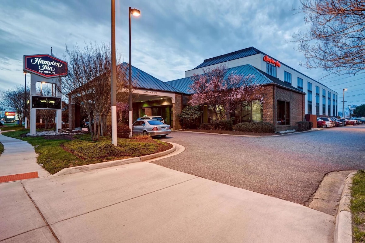Un Hampton Inn by Hilton con entrada despejada, área de estacionamiento y un letrero que indica un despeje de 12 minutos.