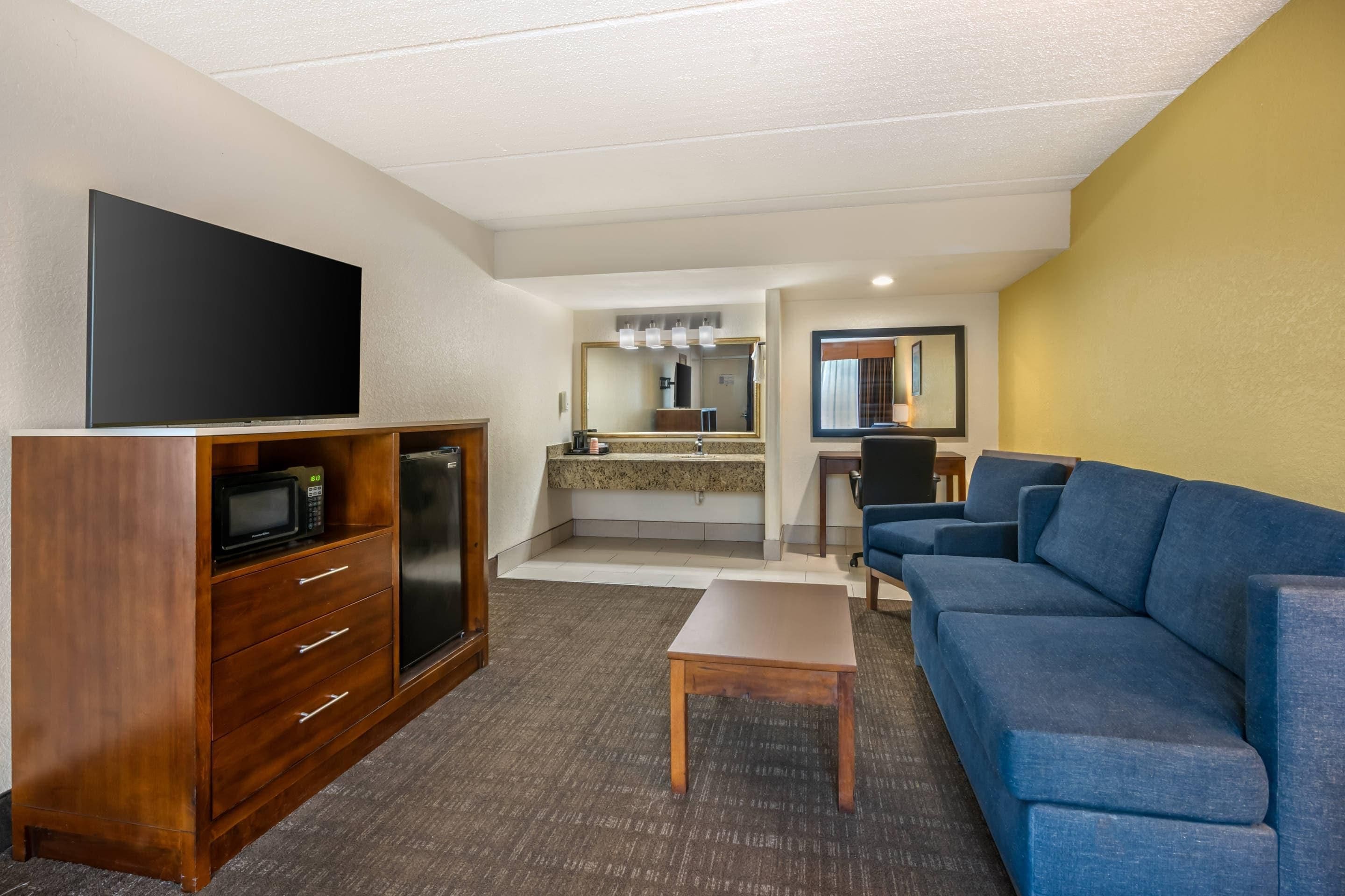 Une chambre d’hôtel équipée d’un téléviseur à écran plat, d’une kitchenette, d’un canapé bleu et d’une petite table.
