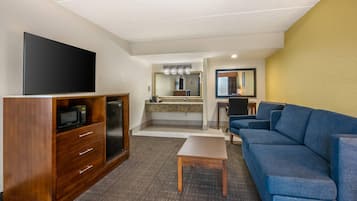 Une chambre d’hôtel équipée d’un téléviseur à écran plat, d’une kitchenette, d’un canapé bleu et d’une petite table.