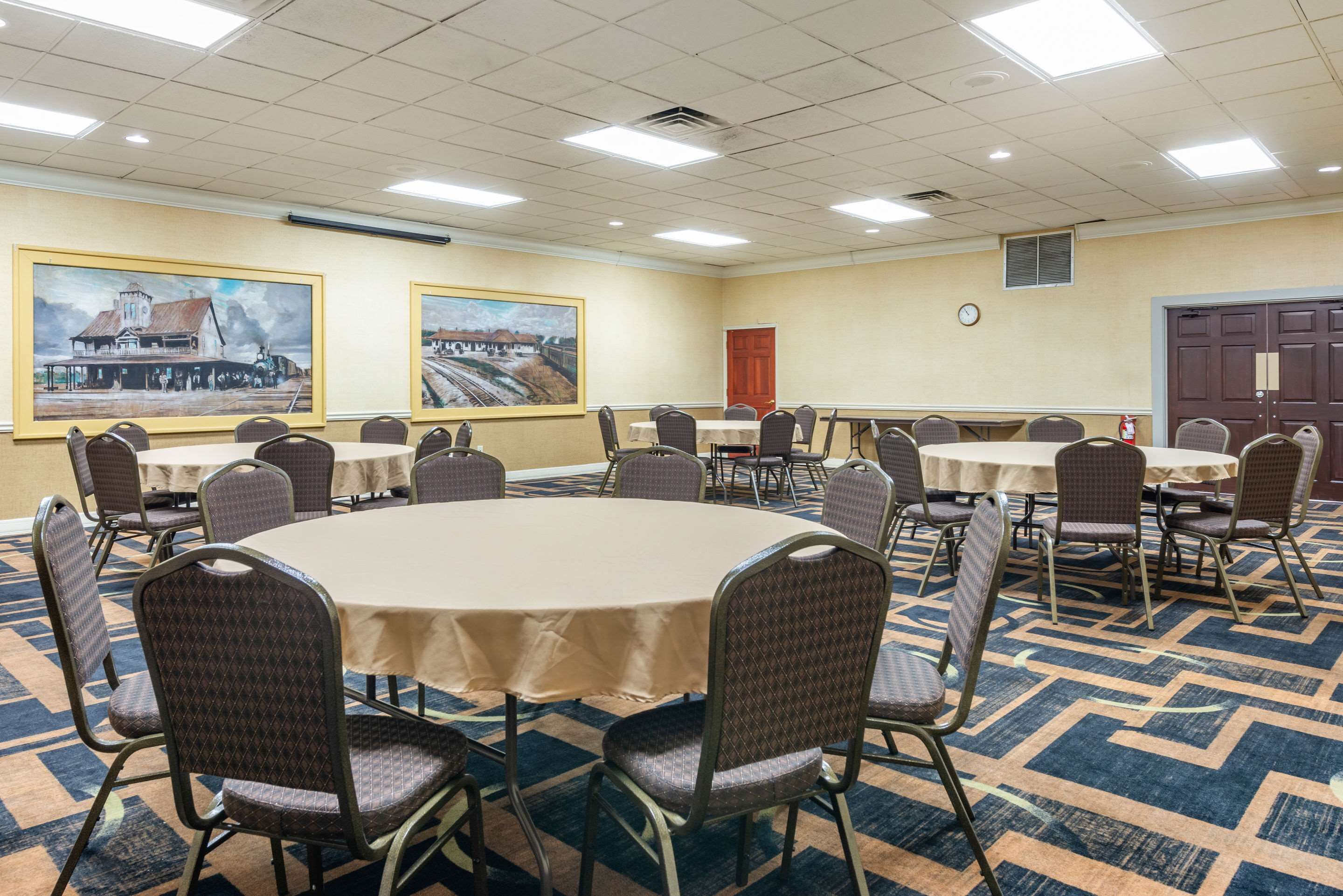 A conference room with round tables and chairs, a clock on the wall, and two large paintings.
