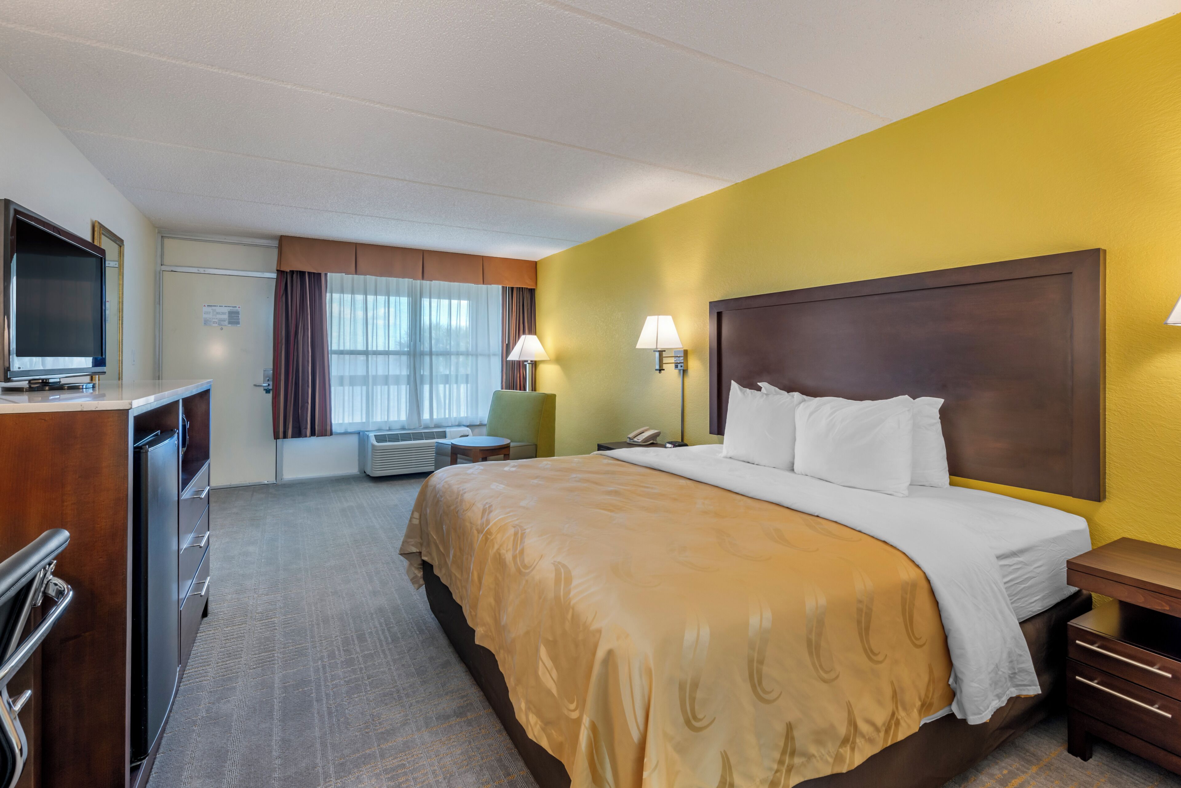 A hotel room with a bed, bedside tables, a desk with a chair, a television, and a window with curtains.