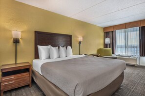A hotel room with a large bed, bedside lamps, a nightstand, a chair, and a window with curtains. - Quality Inn & Suites Palatka Riverfront (Palatka)