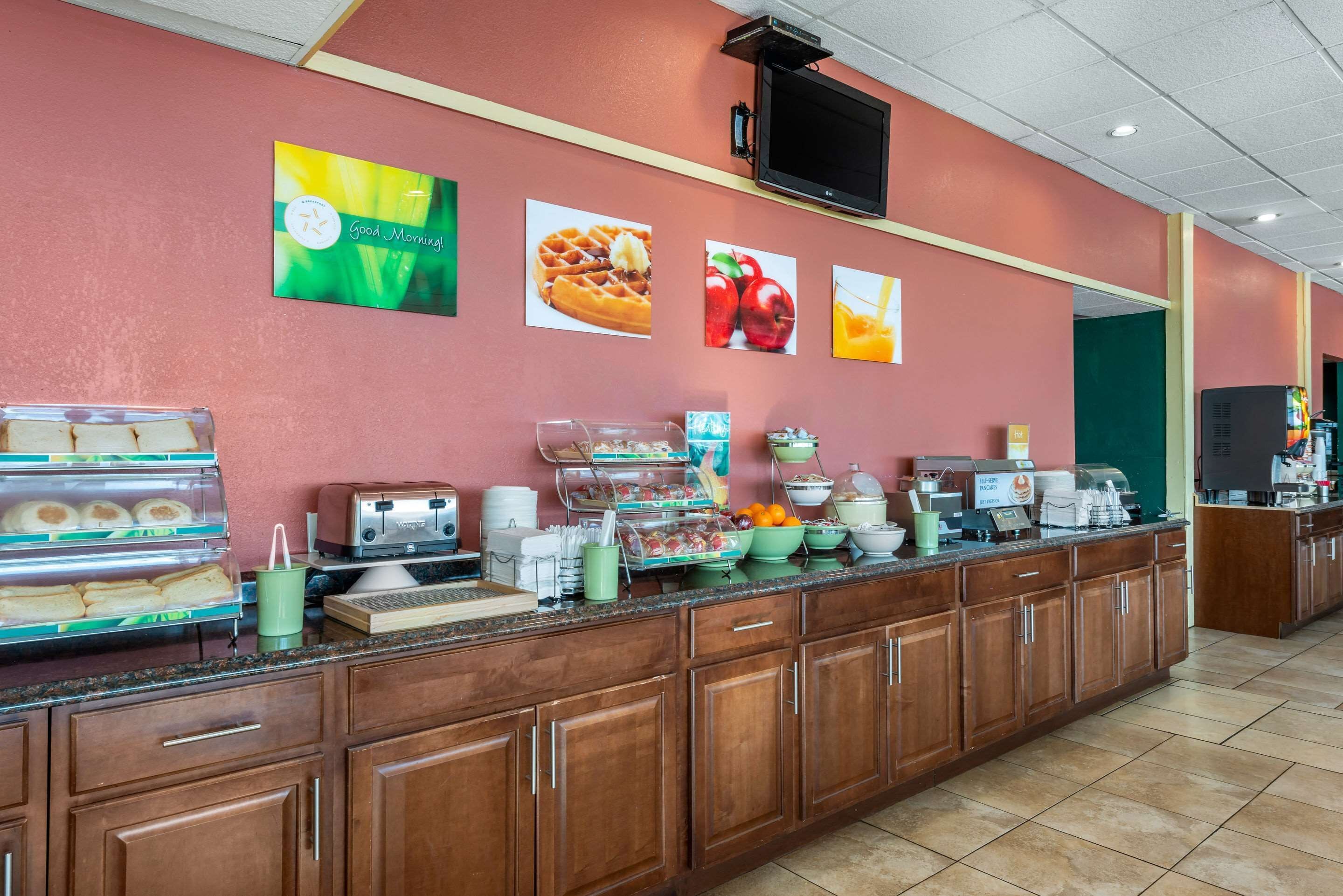 Una barra de desayuno con diferentes alimentos, un televisor montado en la pared y una puerta verde al fondo.