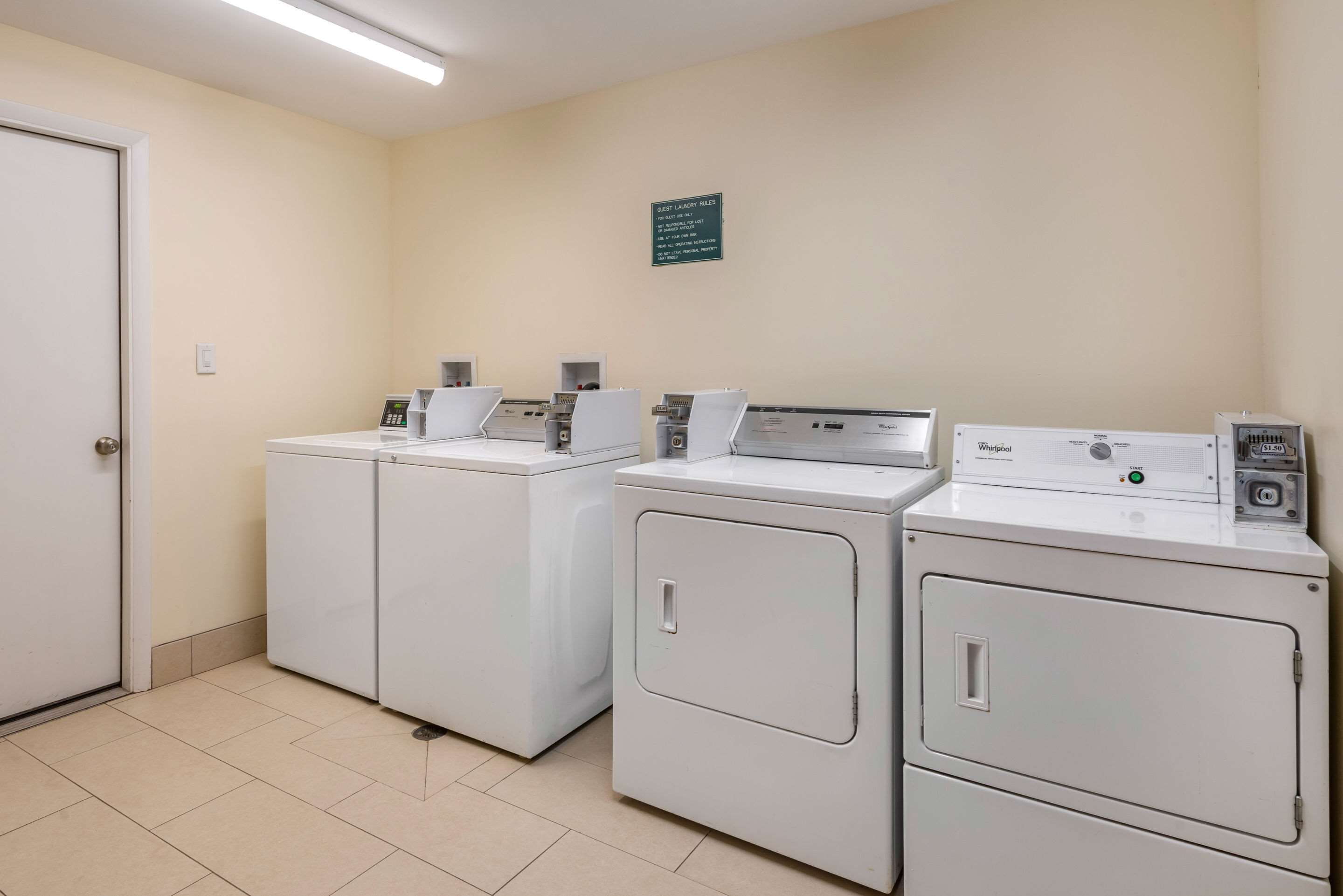 A laundry area with four white washing machines, a door, and a wall-mounted sign.