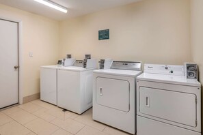 A laundry area with four white washing machines, a door, and a wall-mounted sign. - Quality Inn & Suites Palatka Riverfront (Palatka)