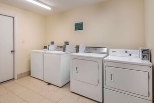 Un área de lavandería con cuatro lavadoras blancas, una puerta y un letrero en la pared.