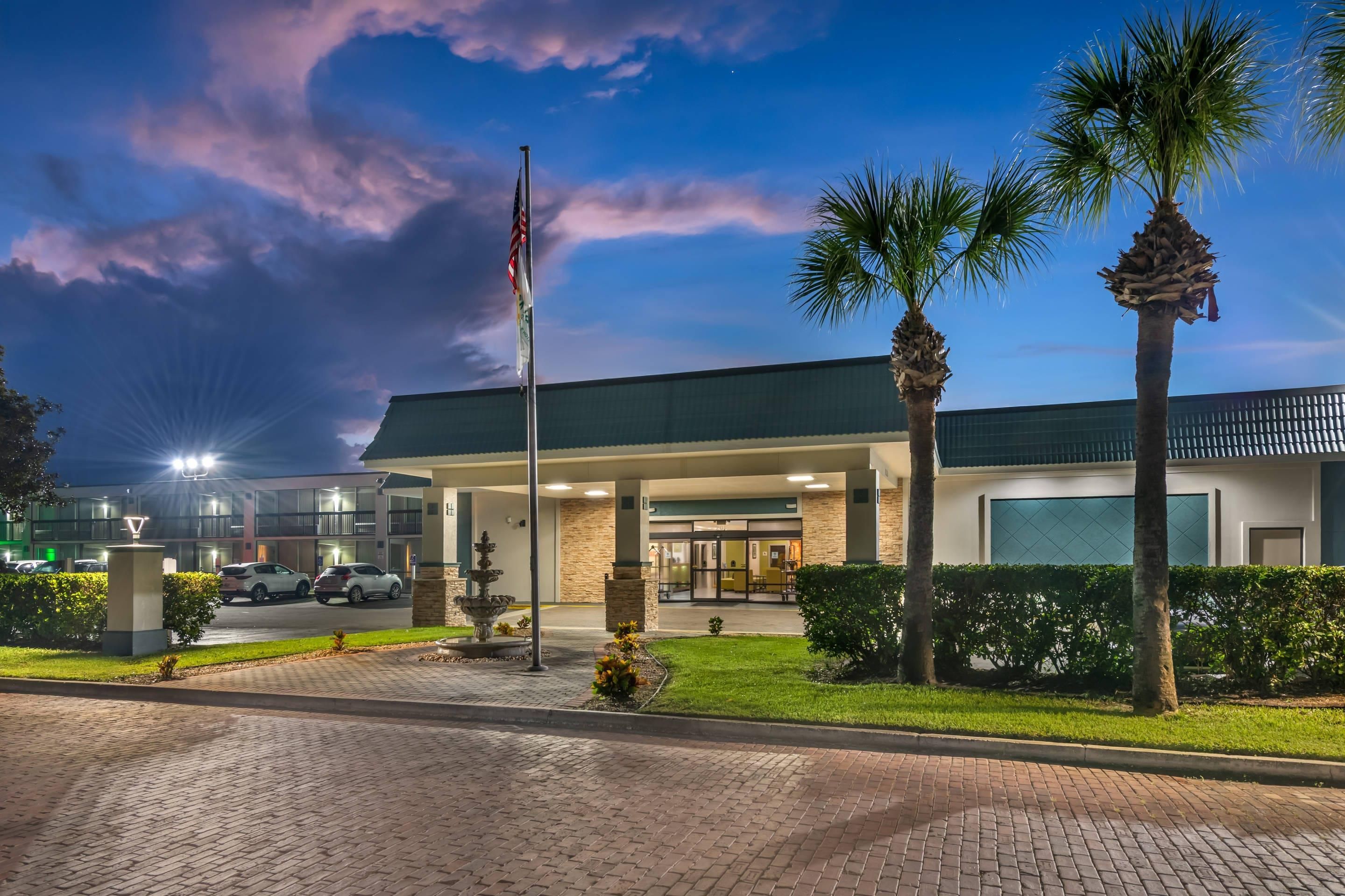 A hotel entrance with a flag, palm trees, and a paved driveway.