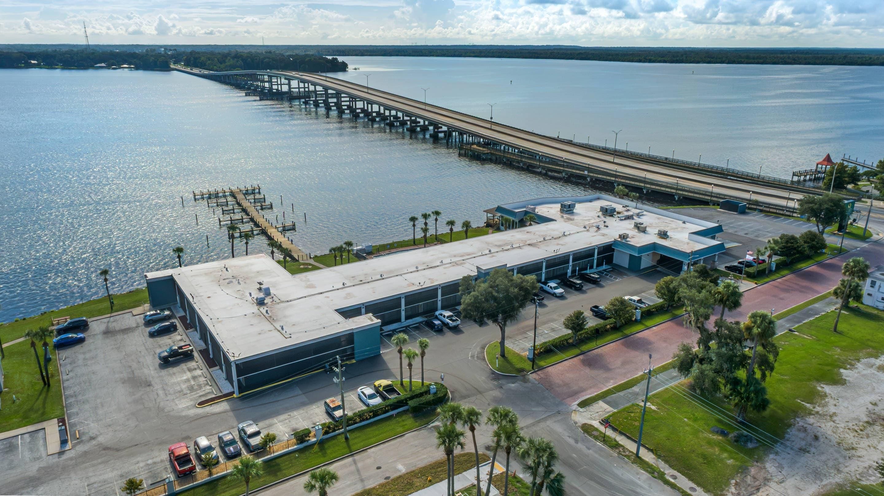 An aerial view of a building with a parking lot, adjacent to a body of water and a pier.