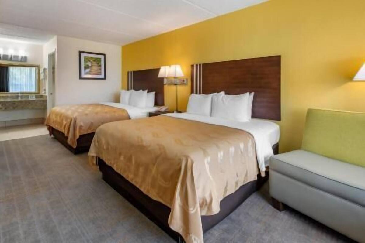 Habitación de hotel con dos camas, un sofá, una lámpara y un cuadro en la pared.