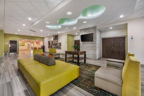 Un hall de hotel con una recepción, un sofá, un sillón y un televisor montado en la pared.