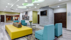 A lobby with a yellow sofa, teal armchairs, a stone accent wall, a flat-screen TV, and a patterned rug. - Quality Inn & Suites Palatka Riverfront (Palatka)