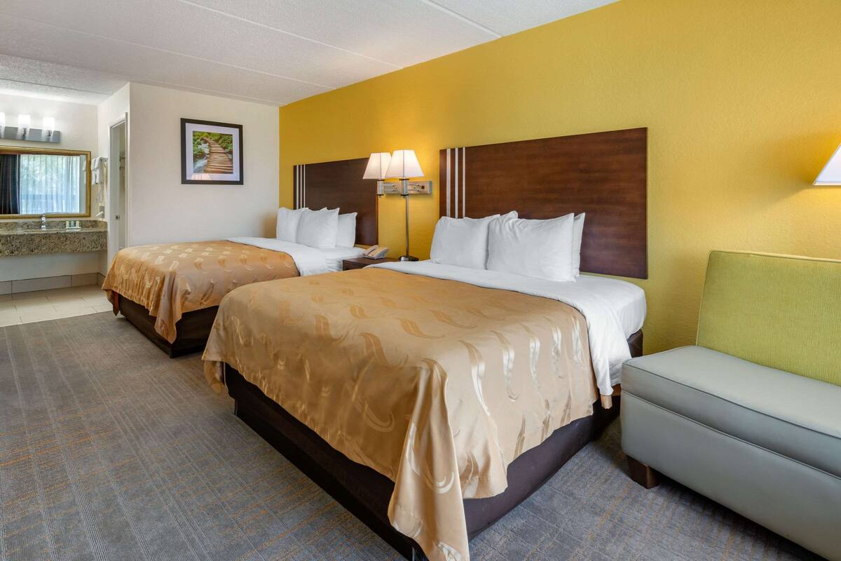 A hotel room with two beds, a sofa, a bathroom, and a hallway.