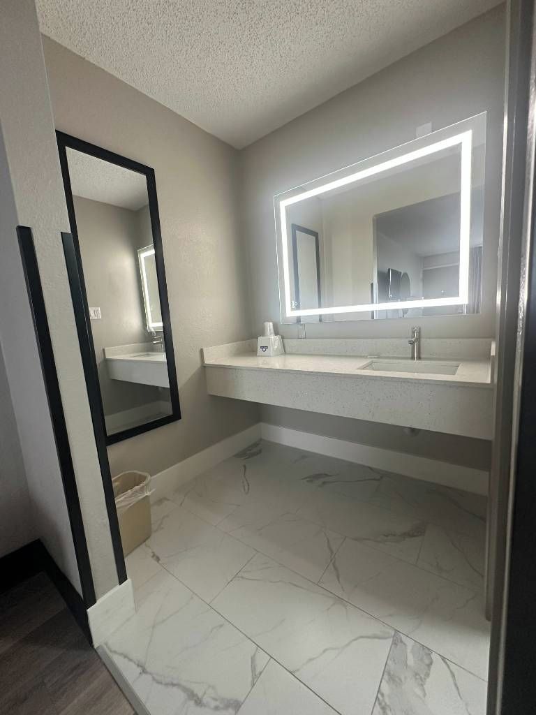 Un baño con lavamanos doble, espejo con luz e incluye un cesto de basura.
