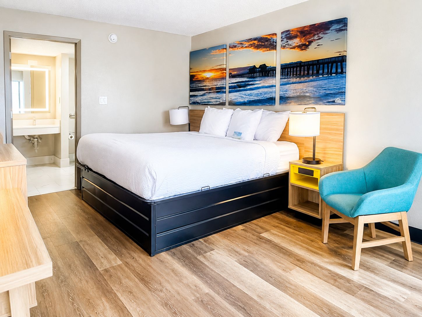 A hotel room with a bed, a chair, a nightstand, and a wall-mounted lamp.