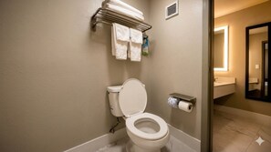Une salle de bain équipée de toilettes, d’un porte-serviettes avec des serviettes pliées et d’un support à papier toilette.