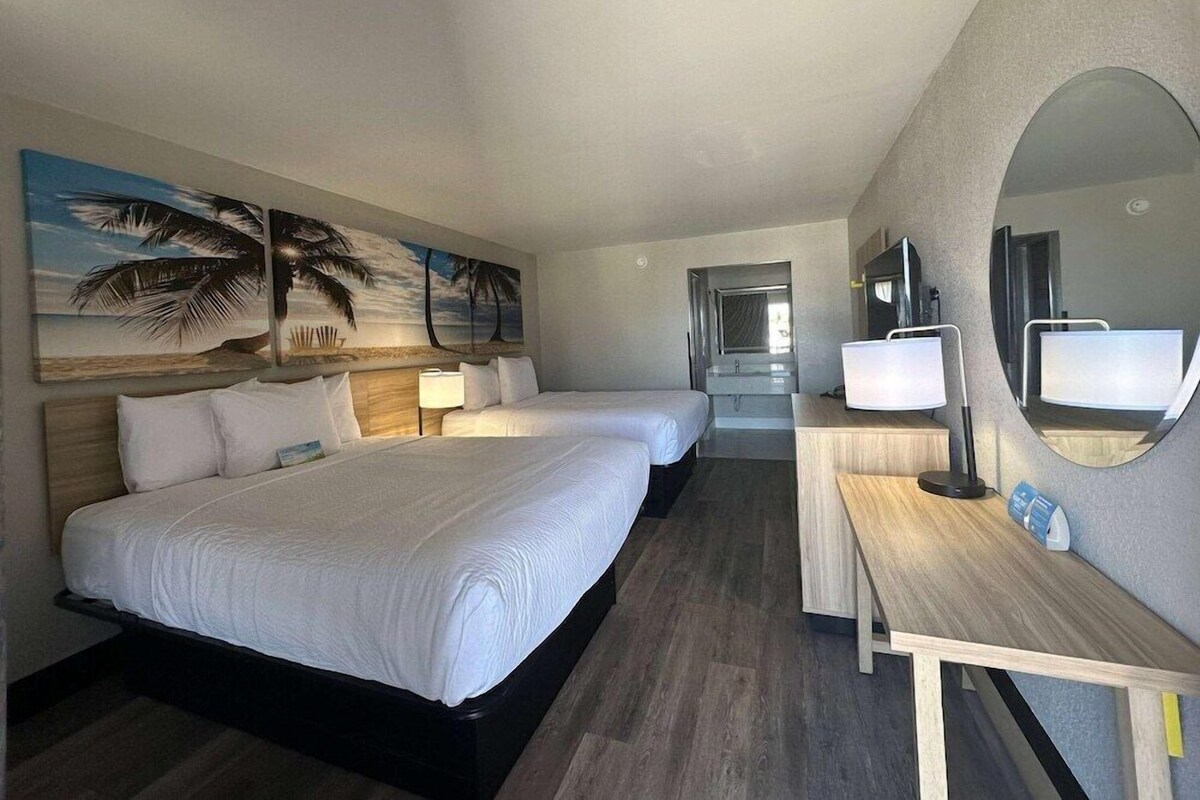 A hotel room with two beds, a desk, a TV, and a large mirror.