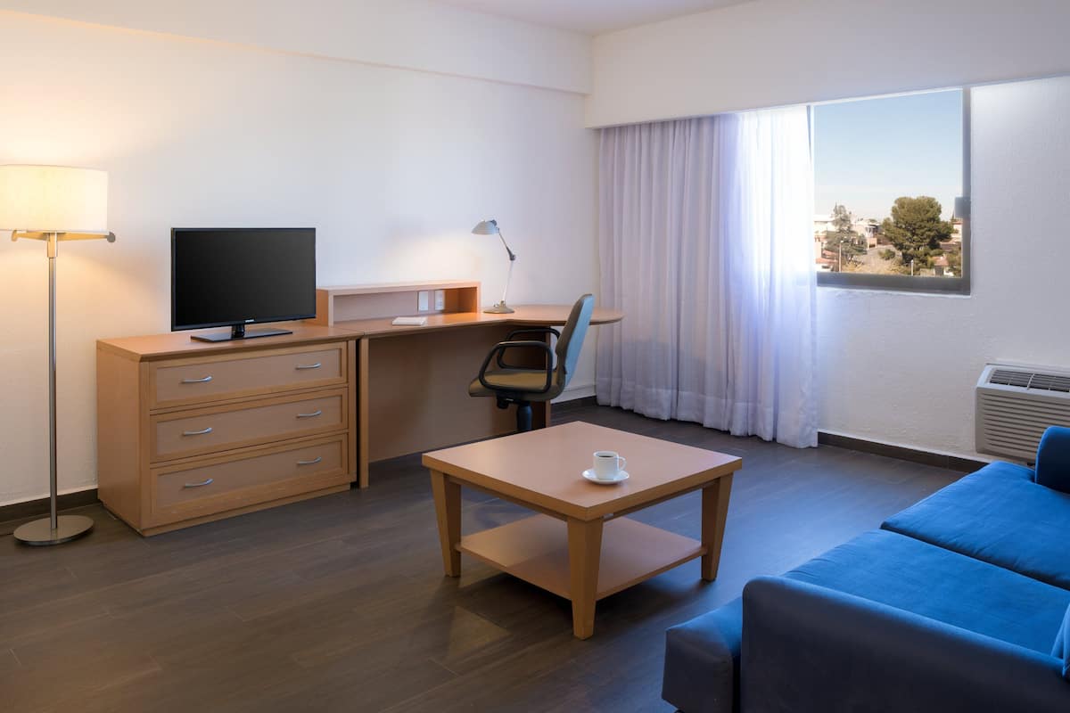 Habitación de hotel con escritorio, silla, televisor y sofá.