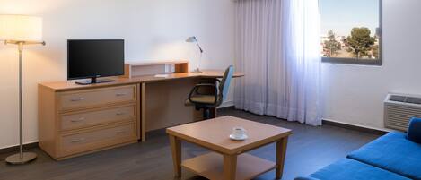 Habitación de hotel con escritorio, silla, televisor y sofá.