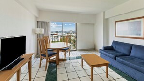 Une chambre d’hôtel avec un balcon, une télévision, un canapé, une table à manger avec des chaises et un tableau au mur.