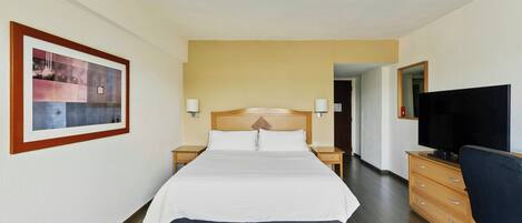 Ein Hotelzimmer mit einem großen Bett, einem Holzkopfteil, Nachttischen mit Lampen, einem Fernseher und einem Schminktisch.
