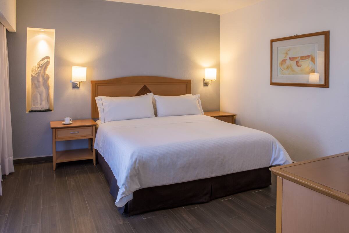 Una cama bien hecha con sábanas blancas, un cabecero de madera y dos lámparas de noche.