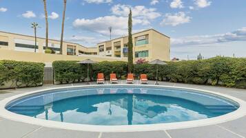 A swimming pool with lounge chairs, palm trees, and a building with multiple floors and balconies.