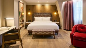 Habitació d'hotel amb un llit gran, una taula de treball, una cadira, un sofà vermell i una finestra amb cortines.
