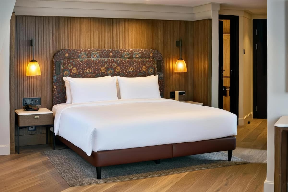A neatly made bed with a patterned headboard, bedside lamps, and a wooden floor.