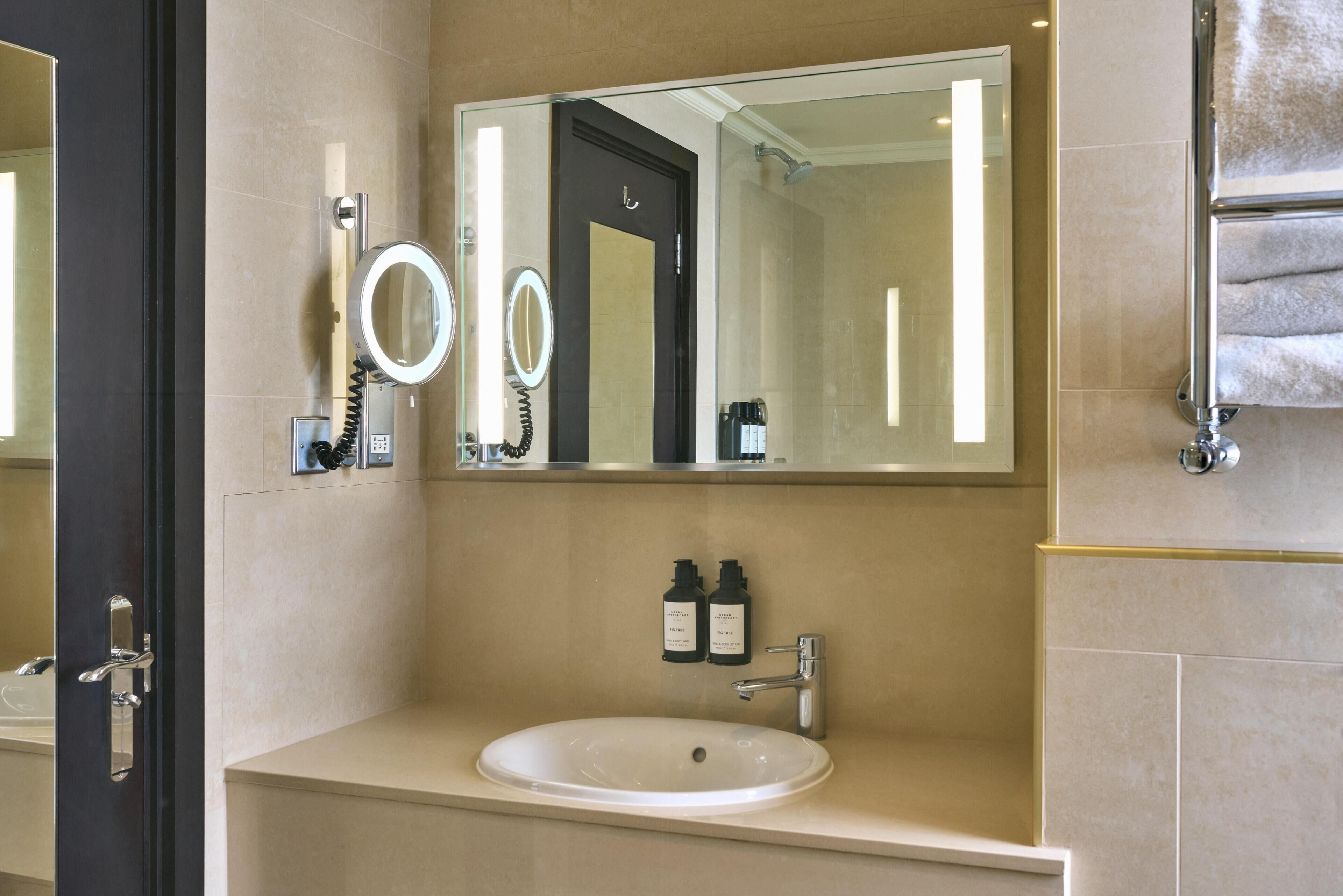 A bathroom with a large mirror, a sink, and a towel rack.
