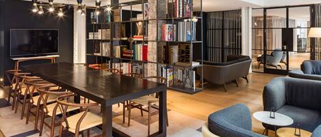 A modern living room with a dark wooden table, multiple chairs, a bookshelf, and a television.